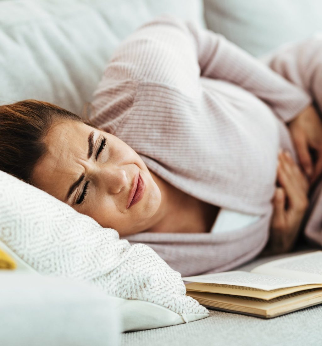 young-woman-feeling-pain-her-abdomen-while-lying-down-sofa-home-min